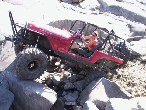 1989 Ford Bronco - A woman drives a red Jeep Wrangler over large rocks on an off-road trail.