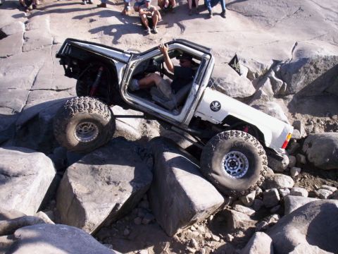 1989 Ford Bronco - A modified off-road vehicle tackles a challenging rocky terrain, with spectators watching from above.