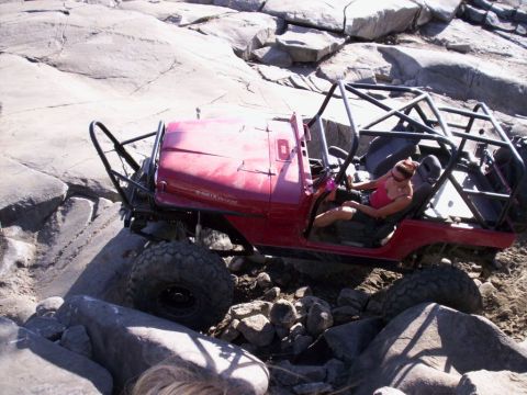 1989 Ford Bronco - This red Jeep Wrangler is equipped with a roll cage and is shown off-roading over large rocks.