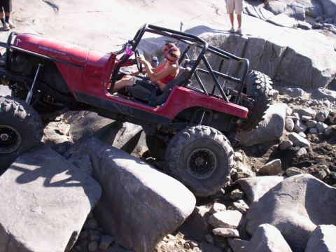 1989 Ford Bronco - A red Jeep navigates a rocky obstacle course with a driver and passenger inside.