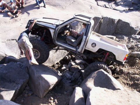 1989 Ford Bronco - A white off-road truck is being maneuvered over large rocks by a person outside the vehicle.