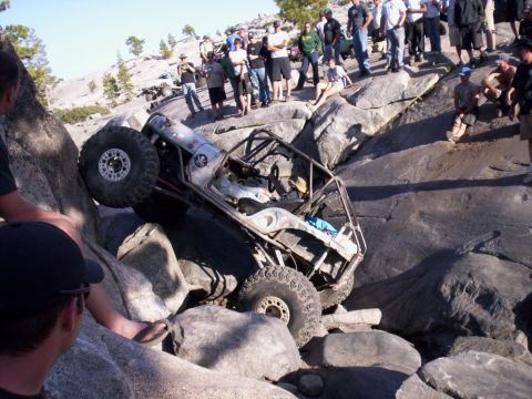 1989 Ford Bronco - A heavily modified off-road buggy navigates a difficult rocky terrain with spectators observing.