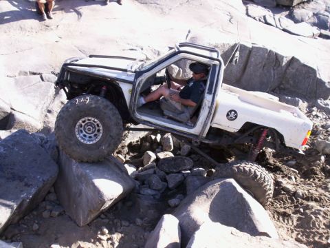 1989 Ford Bronco - A heavily modified white pickup truck navigates a challenging rocky terrain, demonstrating its off-road capabilities.