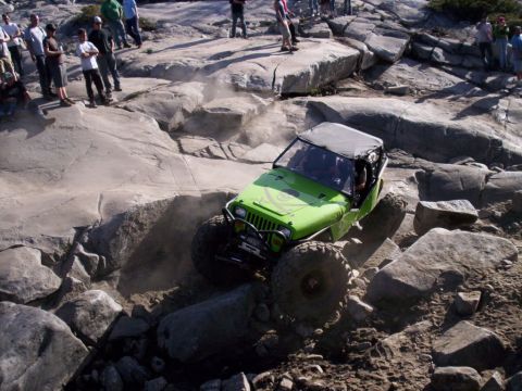 1989 Ford Bronco - Modified Jeep Wrangler navigates a difficult rocky terrain with spectators watching.