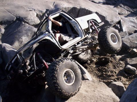 1989 Ford Bronco - A heavily modified off-road vehicle is shown attempting to climb over large rocks.