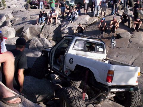1989 Ford Bronco - A group of people watch a modified white pickup truck navigate a rocky terrain.