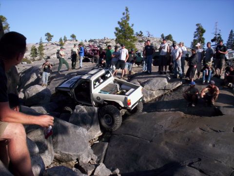 1989 Ford Bronco - A group of people observe a modified pickup truck as it maneuvers through a challenging rocky obstacle course.