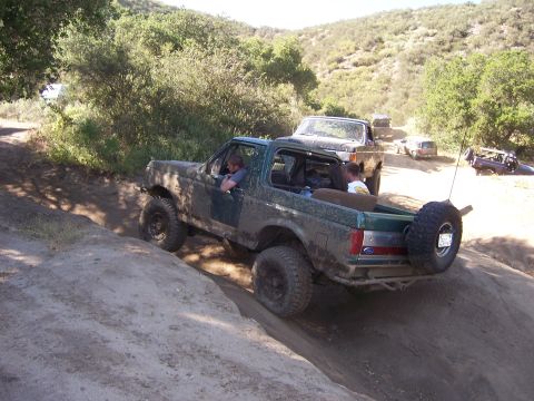 1991 Ford Bronco - A group of vehicles, including a green Ford Bronco, navigate a dirt trail on a sunny day.