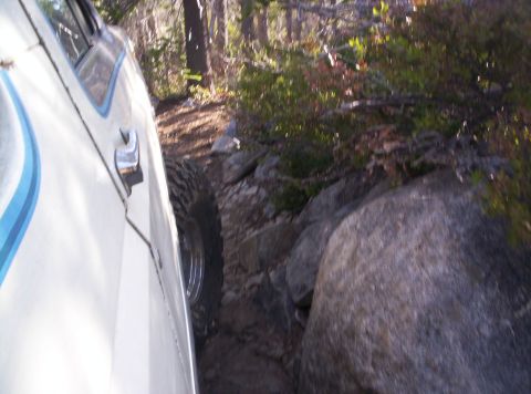 1989 Ford Bronco - A white SUV navigates a challenging rocky path through a forest.