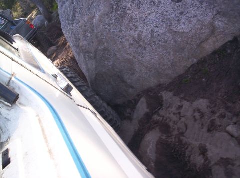 1989 Ford Bronco - A white SUV with a blue stripe is carefully driven between a large boulder and a dirt embankment.