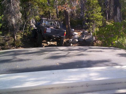 1989 Ford Bronco - Pickup truck with off-road modifications navigating a steep, rocky trail in a wooded area.