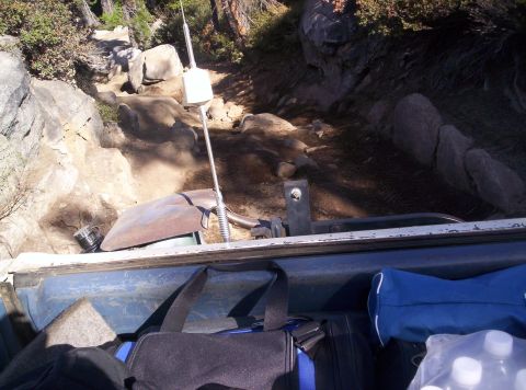 1989 Ford Bronco - A vehicle navigates a challenging off-road path, with bags and water bottles visible in the foreground.