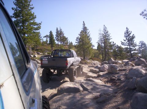 1989 Ford Bronco - Two off-road vehicles navigate a challenging rocky terrain under a clear blue sky.