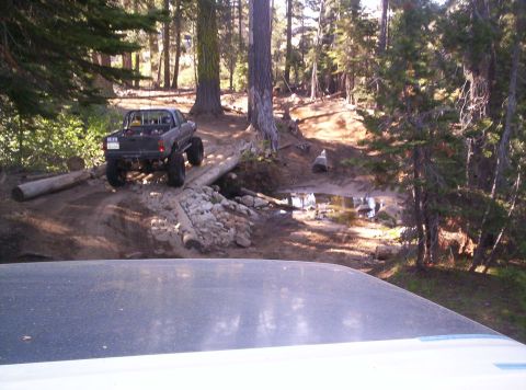 1989 Ford Bronco - A lifted pickup truck navigates a challenging off-road obstacle in a wooded area.