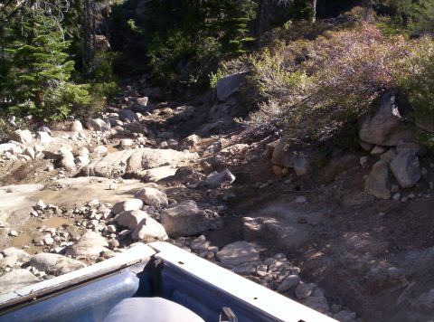 1989 Ford Bronco - Navigating a rocky, uneven trail through a wooded area.