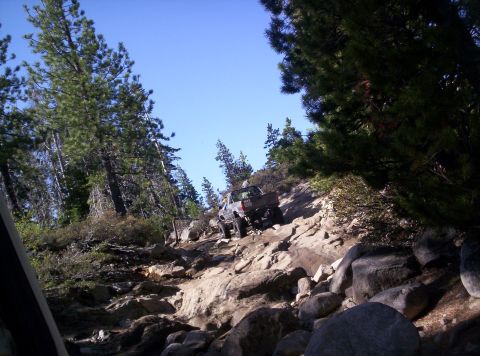 1989 Ford Bronco - A gray pickup truck navigates a challenging rocky incline under a clear blue sky.