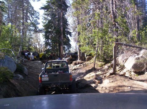 1989 Ford Bronco - Several off-road vehicles navigate a challenging dirt trail through a wooded area.