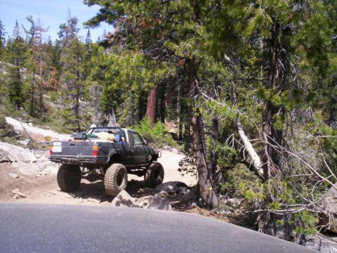 1989 Ford Bronco - A modified pickup truck navigates a challenging off-road path through a forest.