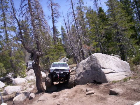 1989 Ford Bronco - Off-road vehicle navigating a challenging rocky path in a wooded area with large boulders.