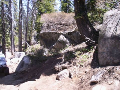 1989 Ford Bronco - A silver SUV is seen traversing a challenging, rocky path through a wooded area with large boulders.