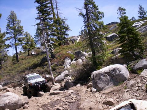 1989 Ford Bronco - Off-road vehicle tackling a challenging rocky path in a mountainous, wooded area.