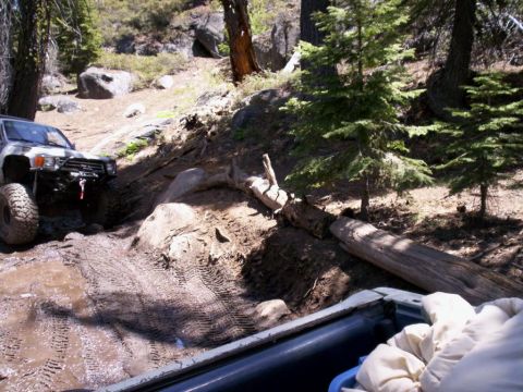 1989 Ford Bronco - An off-road vehicle navigates a muddy trail with a fallen log.