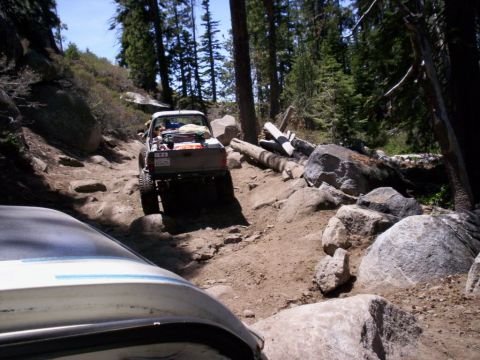 1989 Ford Bronco - A pickup truck navigates a challenging, rocky trail through a wooded area, with another vehicle following behind.