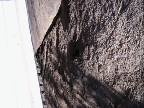 1989 Ford Bronco - A close-up view of a textured rock face, partially obscured by shadows and a white vertical object on the left.