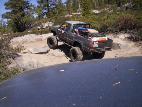 1989 Ford Bronco - A modified pickup truck tackles a challenging off-road trail with large tires and a roll cage.