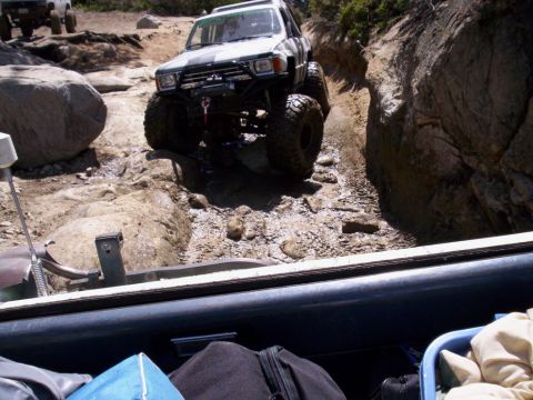 1989 Ford Bronco - An off-road SUV with large tires and a winch navigates a challenging rocky terrain on a sunny day.