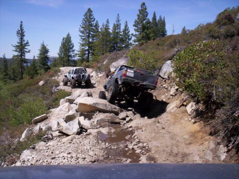 1989 Ford Bronco - Off-road trucks tackle a challenging rocky trail in a mountainous, wooded area.
