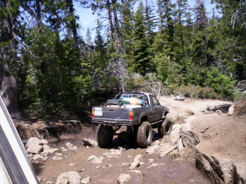 1989 Ford Bronco - A modified pickup truck tackles a challenging off-road path through a forest.
