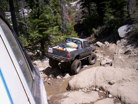 1989 Ford Bronco - A modified pickup truck tackles a challenging off-road course, with another vehicle partially visible in the foreground.