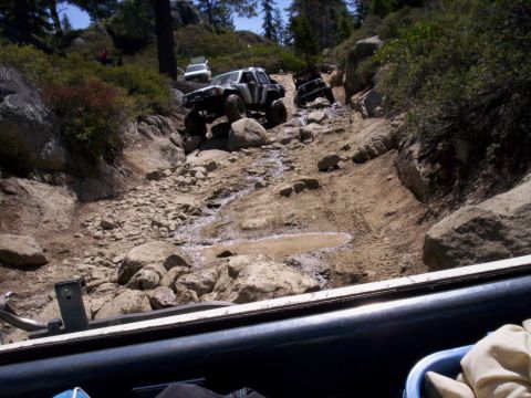 1989 Ford Bronco - Several 4x4 vehicles ascend a challenging off-road course with water and mud obstacles.