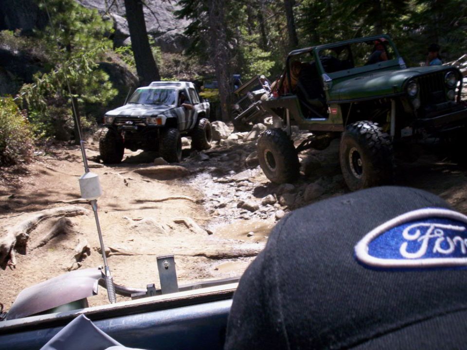 Off-road vehicles navigating a rocky trail. A Ford hat is in the foreground
