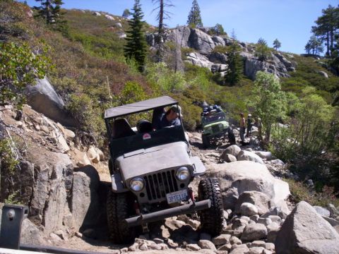 1989 Ford Bronco - Jeeps tackling a challenging rocky trail in a mountainous, wooded area.