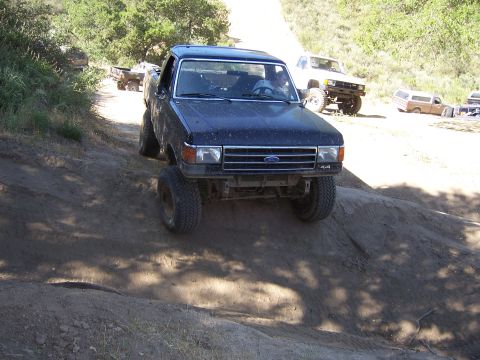 1991 Ford Bronco - A dark blue 1987 Ford F-150 truck navigates an off-road trail with other vehicles in the background.