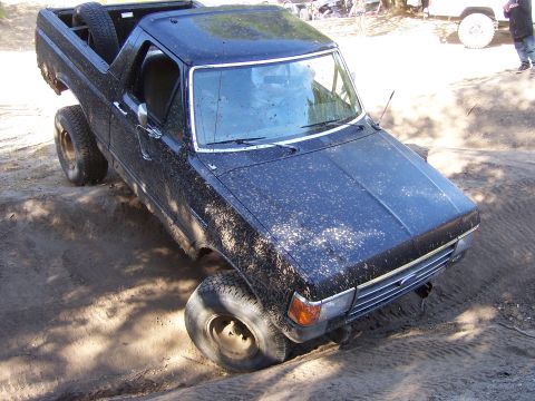 1991 Ford Bronco - This black Ford Bronco is navigating a dirt track with its front right wheel stuck in the mud.