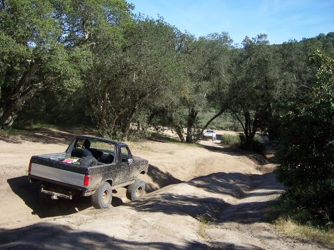1991 Ford Bronco - A black Ford Bronco navigates a challenging dirt path, with another vehicle visible further down the trail.