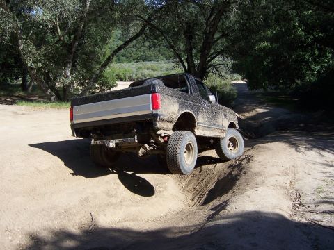 1991 Ford Bronco - A mud-covered 1991 Ford Bronco navigates a challenging dirt trail during an off-road event.