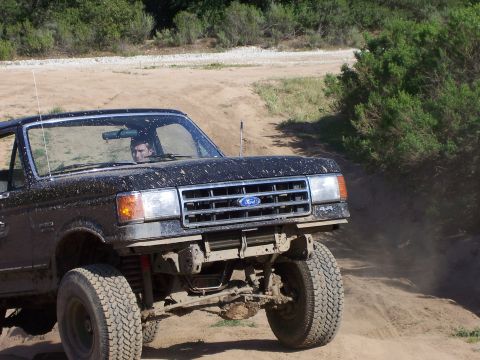 1991 Ford Bronco - A driver navigates a dusty, off-road trail in a black Ford Bronco.