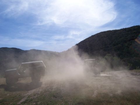 1991 Ford Bronco - Two SUVs navigate a dusty off-road trail under a bright, partly cloudy sky.