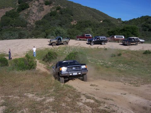 1991 Ford Bronco - Several trucks and SUVs are gathered for an off-road event, with one Ford F-150 kicking up dust.