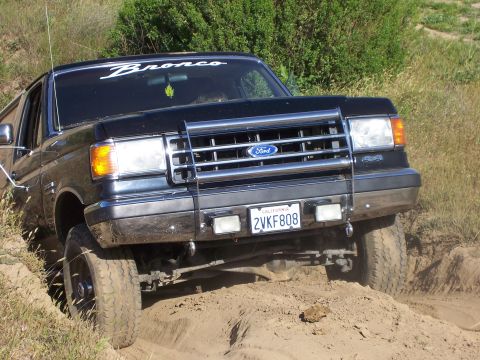1991 Ford Bronco - This 1991 Ford Bronco is navigating a sandy, off-road trail with green brush in the background.