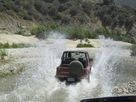 1987 Suzuki Samurai - A red 1987 Suzuki Samurai splashes through a river on a sunny day.