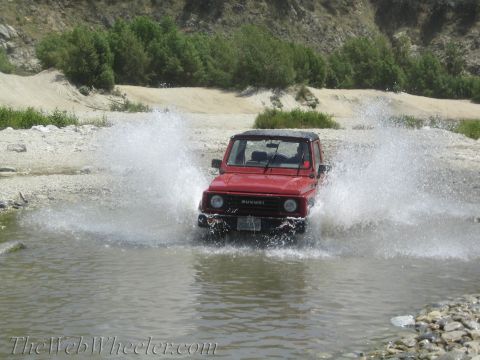 1987 Suzuki Samurai - A red 1987 Suzuki Samurai drives through a shallow body of water, kicking up a large spray.