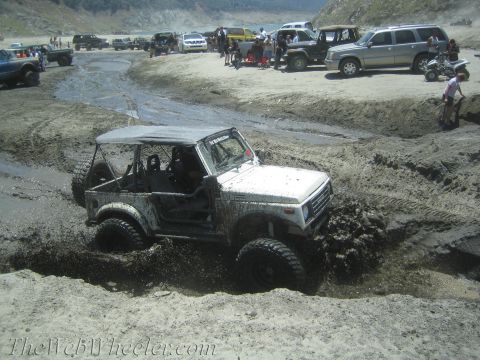 1987 Suzuki Samurai - A white 1987 Suzuki Samurai navigates a muddy terrain, kicking up water and dirt.