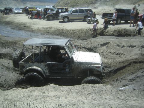 1987 Suzuki Samurai - A white 1987 Suzuki Samurai struggles through a muddy terrain, with other vehicles and spectators in the background.