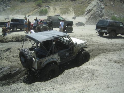 1987 Suzuki Samurai - A white 1987 Suzuki Samurai navigates a muddy off-road course with other vehicles present.