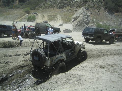 1987 Suzuki Samurai - Several off-road vehicles are gathered in a dusty, muddy area, with one vehicle attempting to navigate through a deep mud pit.